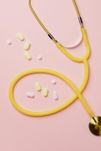 Yellow stethoscope with pills on pink background symbolizing healthcare and diagnosis.